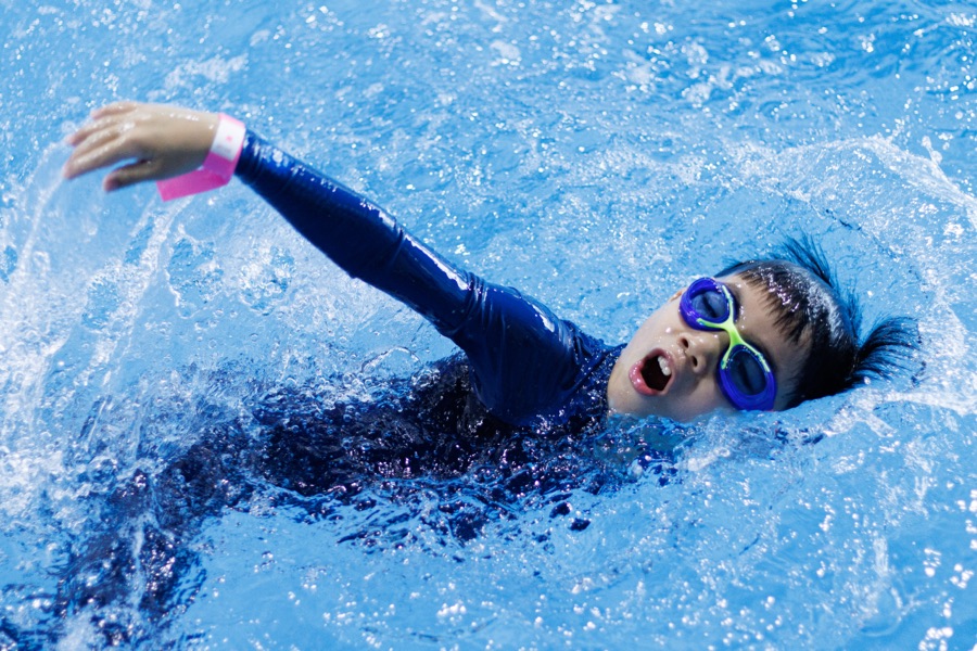 Underwater view of a child swimming freestyle with goggles on, bubbles trailing