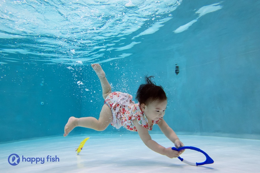 A baby submerged underwater for a moment, eyes open, during a parent-accompanied session