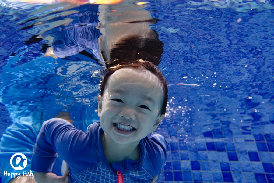 A child smiling underwater with goggles on