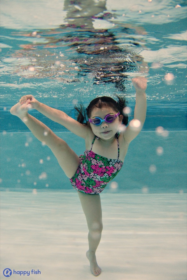 A girl underwater wearing goggles, looking towards the camera