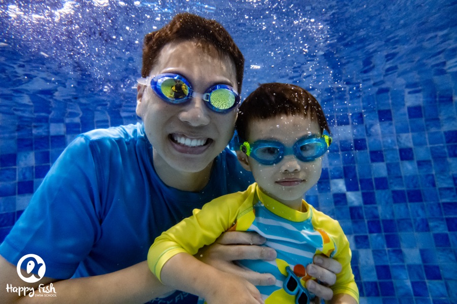 A father and son in goggles side by side in the pool