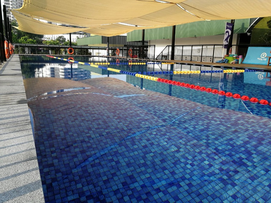 An outdoor lane pool at Happy Fish Jurong East with lane ropes in place, under a shade sail, on a fair-weather day